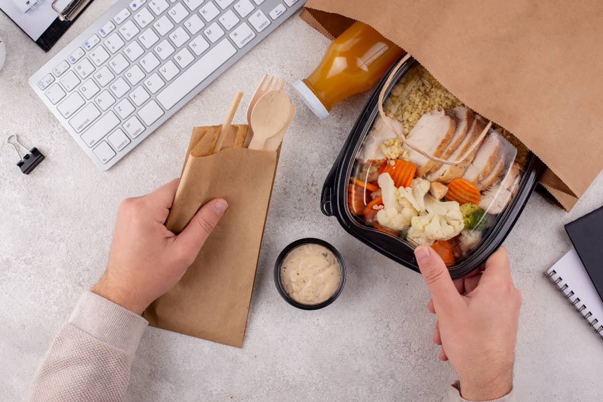 Pessoa organizando uma refeição em embalagens para delivery com talheres sustentáveis, destacando praticidade e cuidado no preparo.