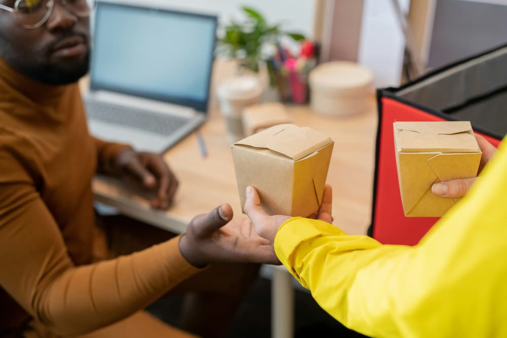 Entregador passando uma embalagem de comida para um cliente em um ambiente de trabalho