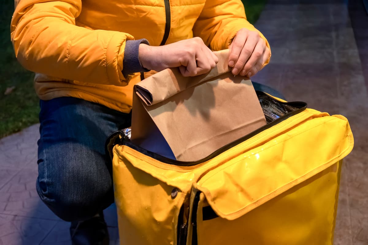 Entregador colocando comida em uma mochila amarela de entrega