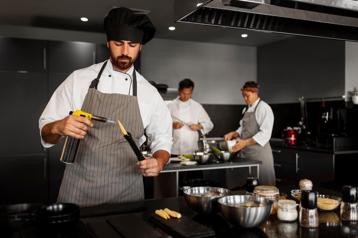 Três chefs em uma cozinha profissional trabalham em pratos refinados, simbolizando o setor de food service em ação.