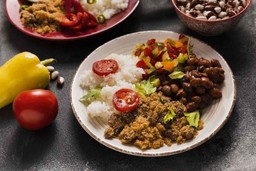 Prato Feito PF com arroz, feijão, farofa, salada colorida e tomate em um prato branco, acompanhado de pimentão e feijão cru.