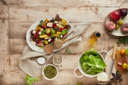 Uma mesa de madeira rústica repleta de ingredientes frescos e naturais, incluindo uma salada colorida com folhas verdes, tomates cereja amarelos e vermelhos, fatias de pêssego e pedaços de queijo em um prato branco.