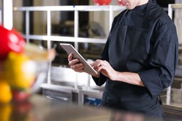 Chef usando tablet na cozinha para controle de custos e aumento da margem de lucro de um restaurante.