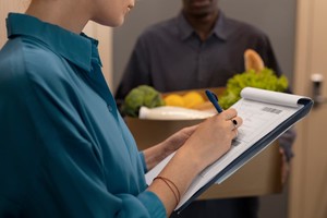 Entrega de comestibles mientras una mujer firma un recibo, ilustrando el impacto de los precios dinámicos en el delivery.