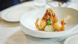 Prato gourmet inspirado em cozinha contemporânea com camarões crocantes, decorado com fatias de pepino e molho cremoso
