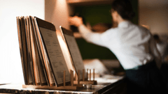 Há uma fileira de cardápios (menus) com acabamento em madeira, organizados verticalmente em suportes sobre um balcão de mármore escuro. O foco está bem nítido nos primeiros menus.