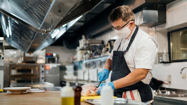 Rentable: hombre de pie con delantal, bata blanca y máscara, cocinando