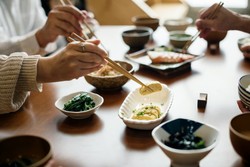 Personas utilizando palillos para comer en una mesa con platos de comida variada