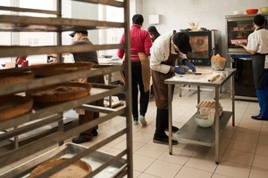 A imagem mostra uma cozinha profissional com várias pessoas trabalhando na preparação de alimentos, lembrando bastante o modelo de uma dark kitchen — também conhecida como cozinha fantasma ou cozinha virtual.