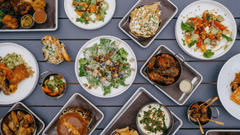 apresenta uma mesa cinza escura vista de cima, repleta de diversas opções culinárias dispostas de forma organizada.