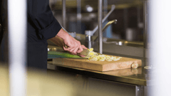 Esta imagem foca no trabalho de precisão e na técnica de um profissional de culinária em uma cozinha industrial.