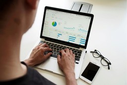 Análise de gráficos de pesquisa de satisfação em laptop com óculos e smartphone ao lado.