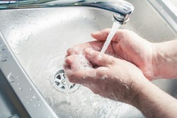 pessoa lavando as mãos em uma pia de aço inoxidável, com água corrente e sabão, formando espuma.