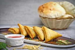 Comida indiana: samosas indianas crocantes e recheadas com especiarias, servidas em uma tábua de madeira rústica.
